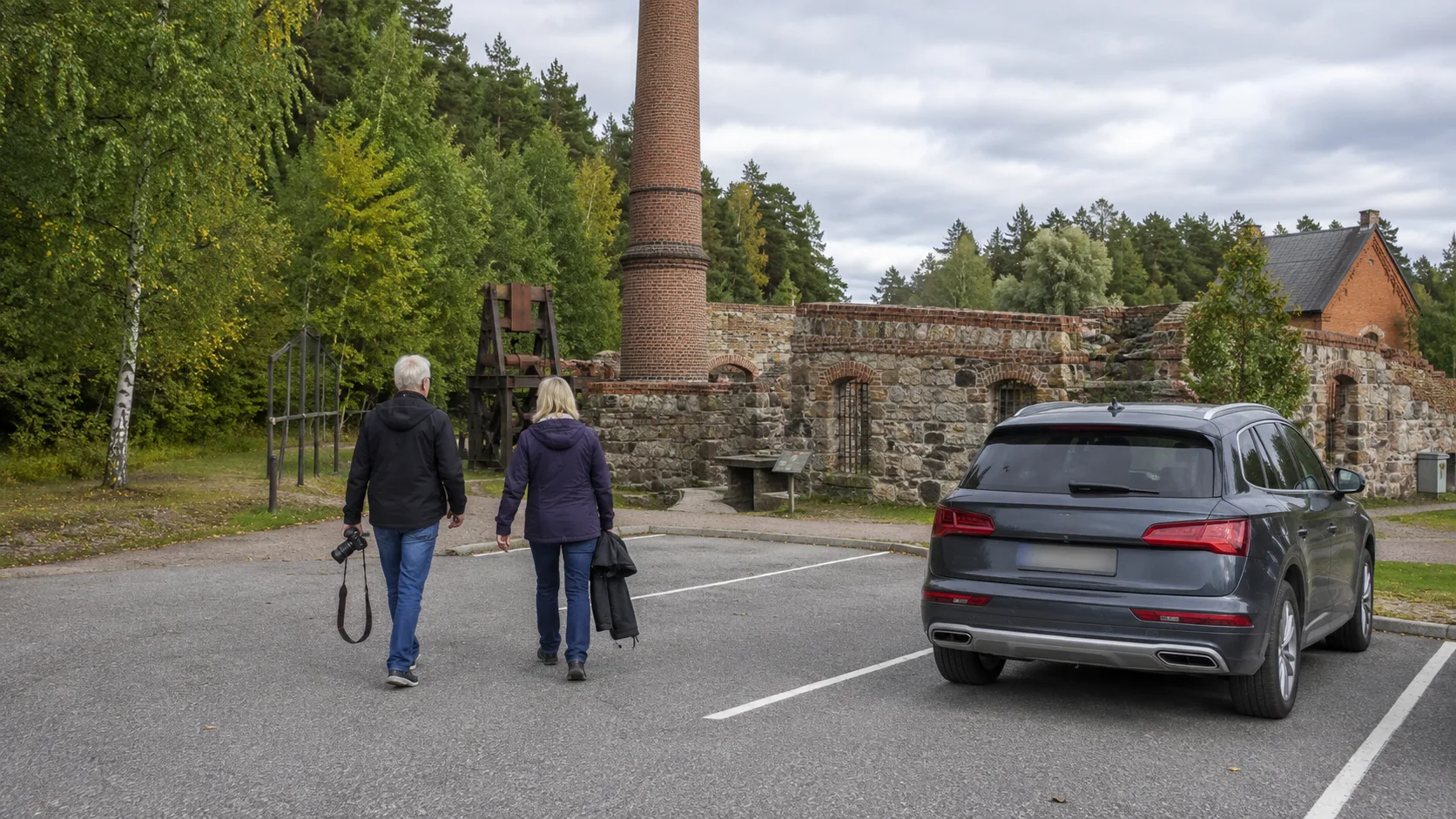 Two travellers walking from a parked car towards a Swedish historic industrial site