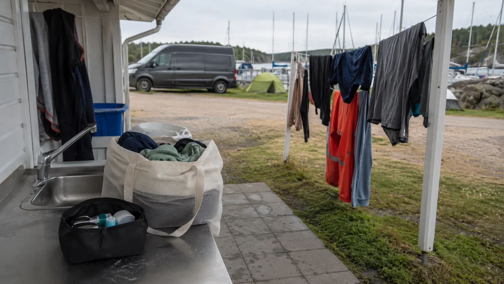 Laundry and towels drying at a marina with a van and sailing boats behind