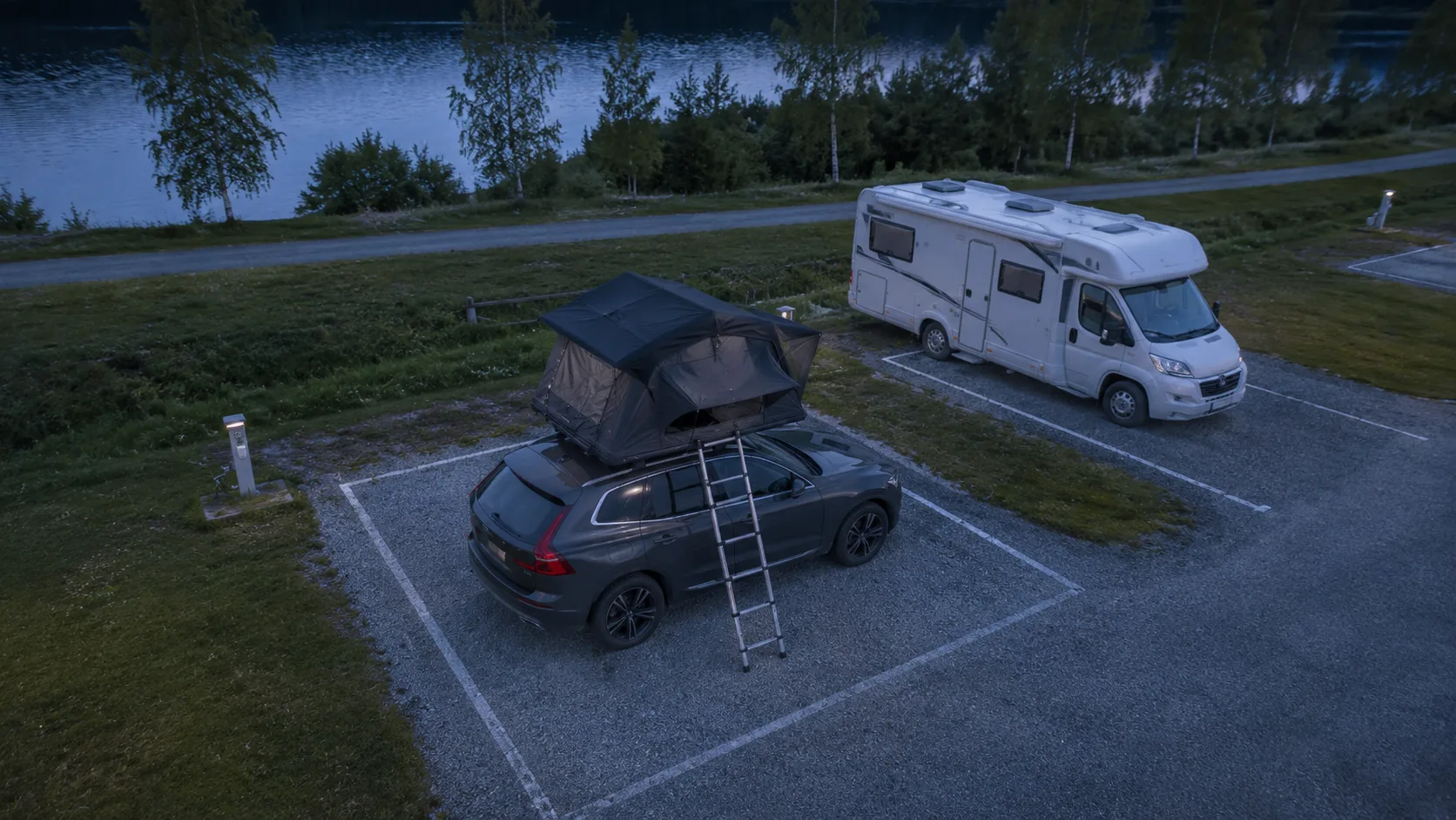 A car with an opened rooftop tent and ladder contained within a marked gravel pitch