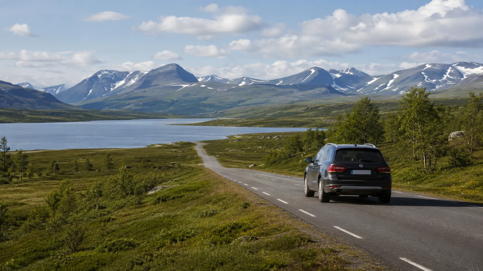 A car driving through Jämtland mountains with a lake and snow-covered peaks behind