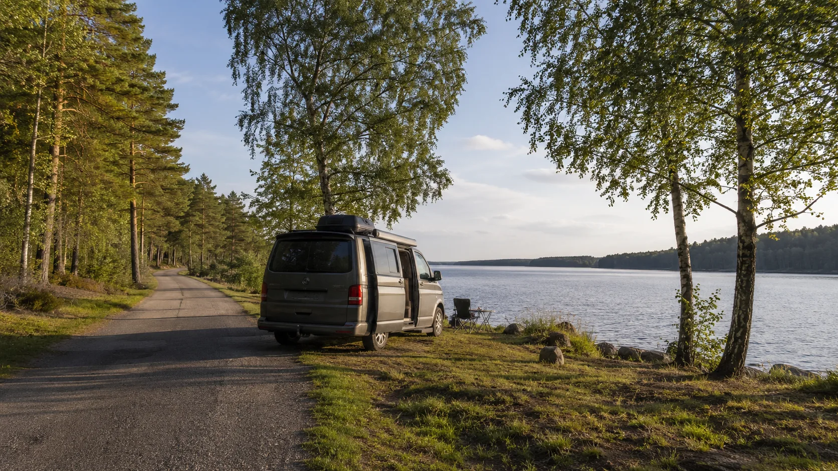 Van parkerad vid stilla sjö och skogsväg i Värmland i kvällsljus