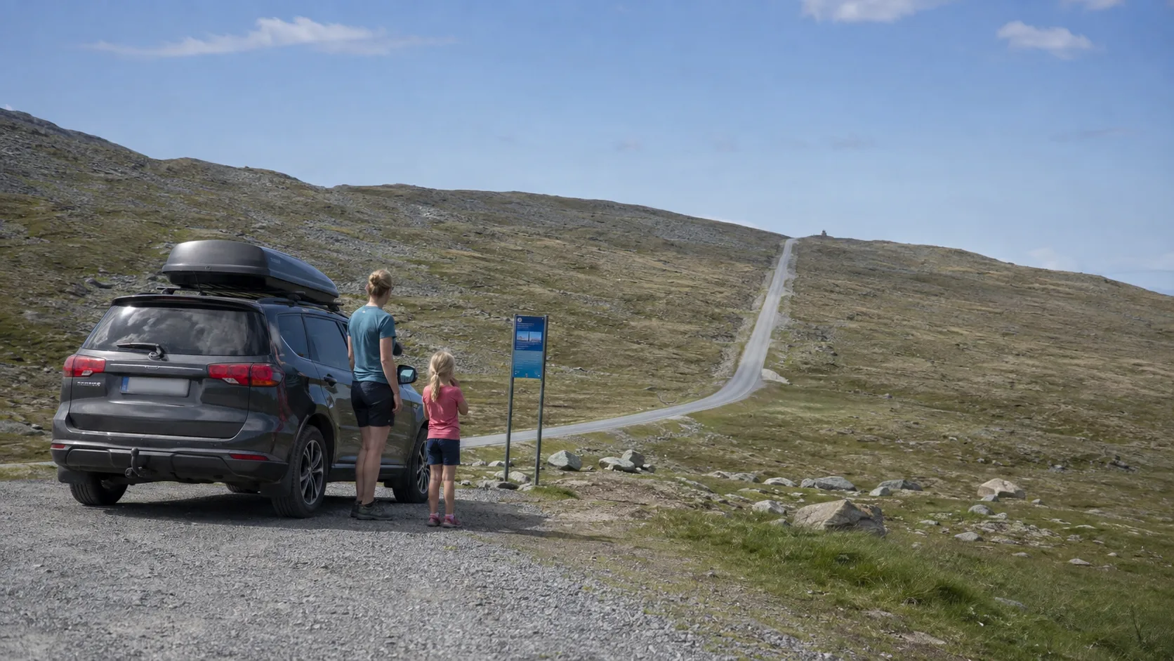An adult and child beside a car and the Trollvägen sign on Nipfjället